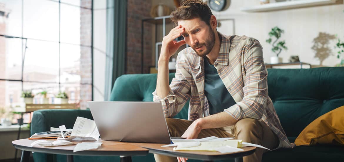 Stressful Accounting at Home: Man Using Laptop, Filling Tax Forms. Worried Male Has Paperwork Problems with Bills and Invoices. Budget Deficit, High Inflation, Financial Difficulty, Debt, Bankruptcy