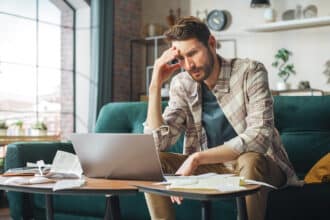 Stressful Accounting at Home: Man Using Laptop, Filling Tax Forms. Worried Male Has Paperwork Problems with Bills and Invoices. Budget Deficit, High Inflation, Financial Difficulty, Debt, Bankruptcy