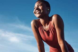 Fitness, black woman and happy athlete smile after running, exercise and marathon training workout. Blue sky, summer sports and run of a African runner breathing with happiness from sport outdoor